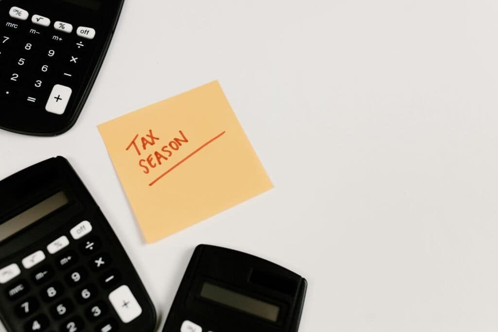 A yellow sticky note with the word tax season on it sits next to two calculators.